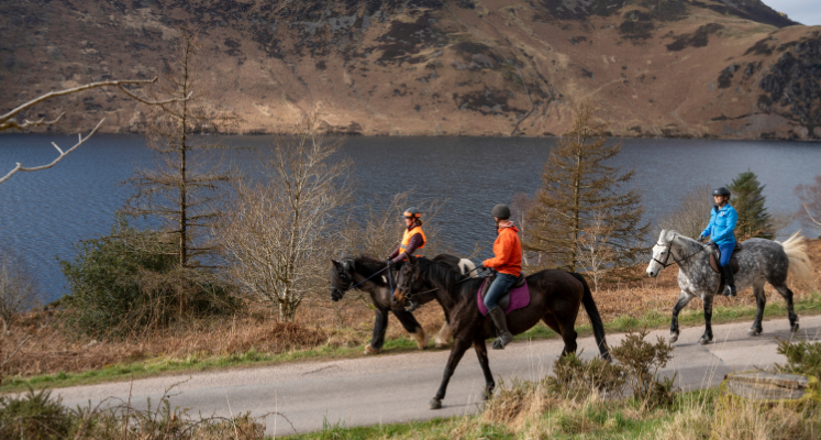 Three horses with riders going along the lakeshore of Ennerdale