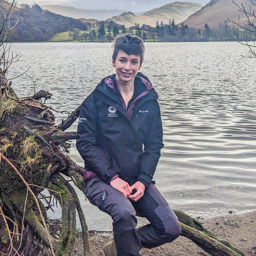 Marnie Calvert sat on a tree in front of a lake smiling