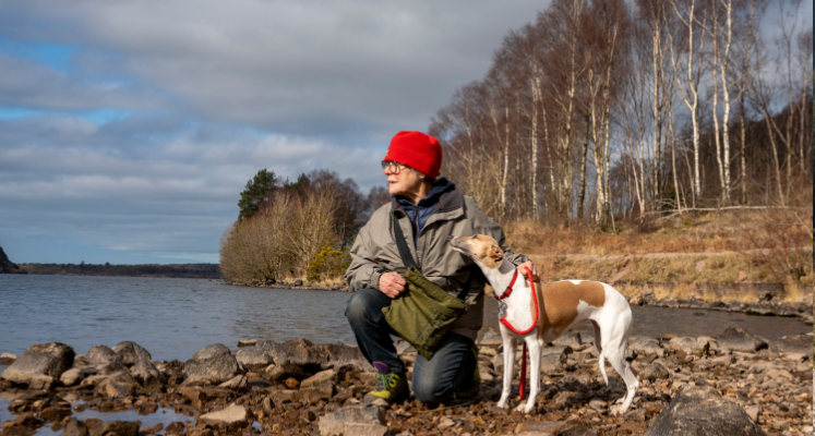 Women crouched down with her dog on the shore of Ennerdale lakeshore