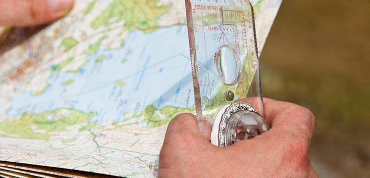 A hand holding a paper map and plastic compass
