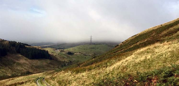 Pylons in the distance of a stoney track in a valley