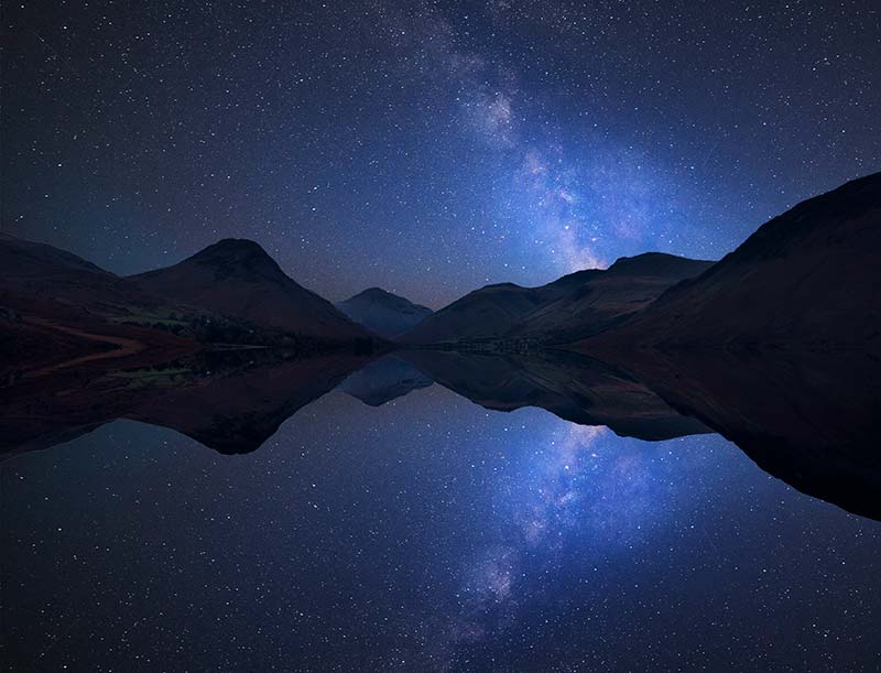 Dark Starry skies above mountains reflected in a lake below