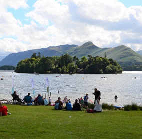 People enjoying the sunshine next to a clear lake.