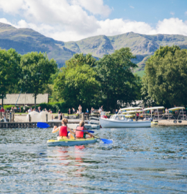 A summery scene at Coniston Boating Centre from the water with two people kayaking towards the shore 