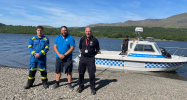 Coastguard, LDNPA Lake Ranger and Cumbria Fire and Rescue Service representatives stand on the shore of Coniston in front of the LDNPA Lake Ranger boat