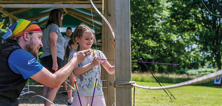 Activity leader helping child with archery bow and arrow