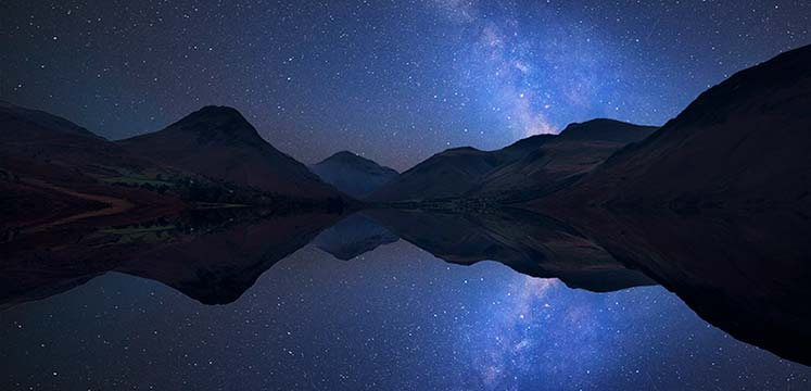 Dark Starry skies above mountains reflected in a lake below