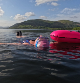 swimmer floating on her back with bright cap and  tow float for visibility