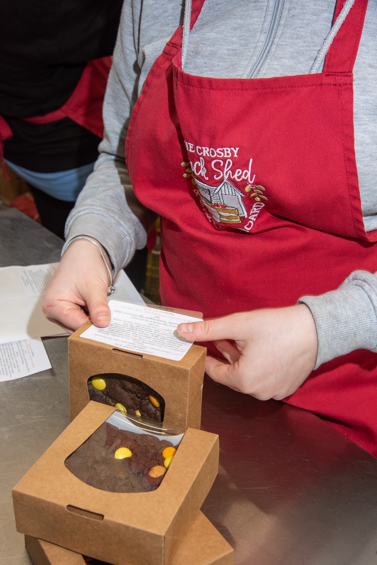 Person in a red apron placing a label on a box, which has a cookie inside.