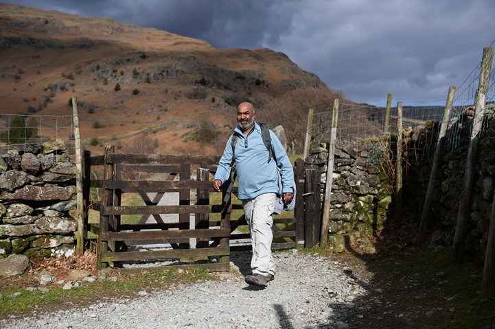 A man walking through a gate on a Lake District track.