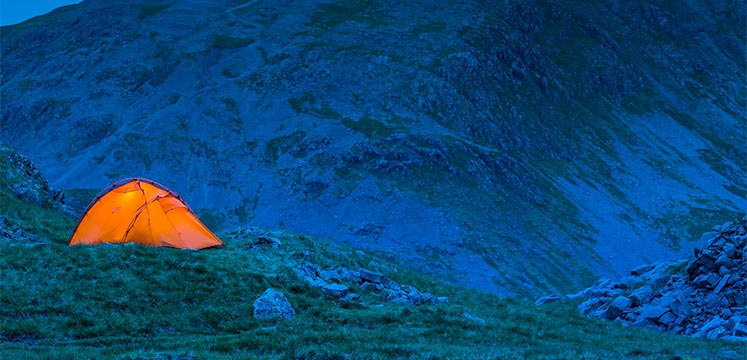 A bright orange tent wild camping on a dark mountainside