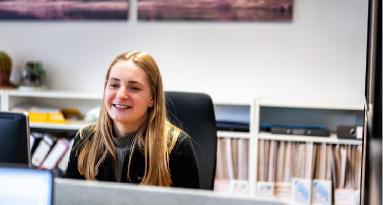 Female colleague sat behind desk smiling at other colleagues
