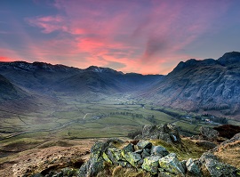 Taken at the top of a valley in the Langdales - the sun is setting and the sky is pink, the valley is green and surrounded by fells.