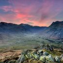Taken at the top of a valley in the Langdales - the sun is setting and the sky is pink, the valley is green and surrounded by fells.